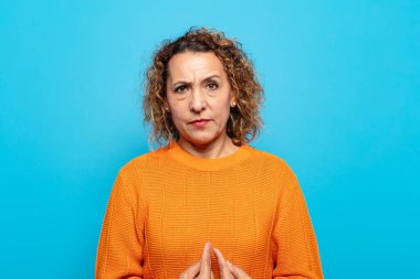 Orta yaşlı bir kadın, şaşkın ve tuhaf bakışlarıyla kendini işaret ediyor. Seçildiğine şaşırmış ve şaşırmış.