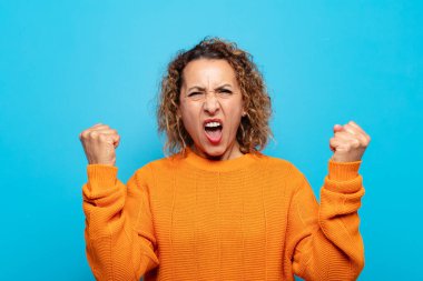 Orta yaşlı bir kadın sinirli bir ifadeyle ya da yumruklarıyla başarıyı kutlarken agresif bir şekilde bağırıyor.