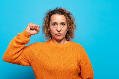 Orta yaşlı kadın ciddi, güçlü ve isyankar hissediyor, yumruğunu kaldırıyor, protesto ediyor ya da devrim için savaşıyor.