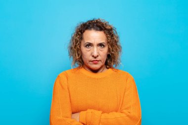 Orta yaşlı bir kadın mutsuz ve hayal kırıklığına uğramış, ciddi görünüyor, kızgın ve kollarını kavuşturmuş.