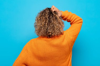 Orta yaşlı bir kadın bilgisiz ve kafası karışık, bir çözüm düşünüyor, eli kalçasında, diğeri kafasında, dikiz aynasından.