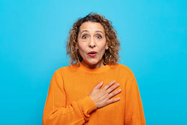 Orta yaşlı bir kadın şaşkın ve şaşırmış hissediyor, gülümsüyor, el ele tutuşuyor, o olmaktan mutlu ya da minnettarlık gösteriyor.