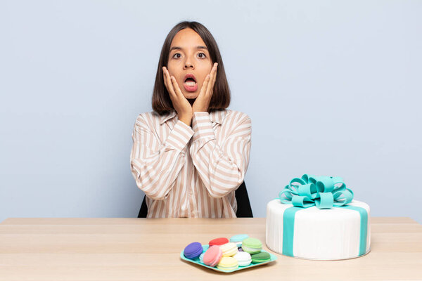 hispanic woman feeling shocked and scared, looking terrified with open mouth and hands on cheeks