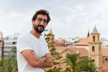 Genç sakallı adam dışarıda poz veriyor.