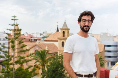 Genç sakallı adam dışarıda poz veriyor.