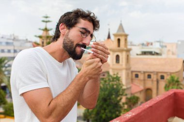 Genç sakallı adam sigara içiyor.