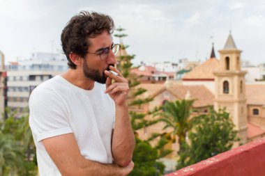 Genç sakallı adam sigara içiyor.