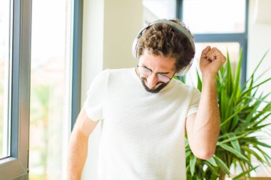 Genç sakallı adam kulaklıklarıyla müzik dinliyor.