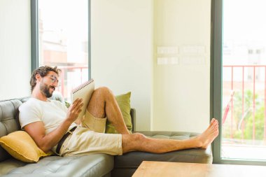 Genç adam evde kitap okuyor.