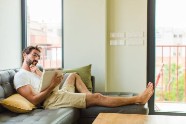 Genç adam evde kitap okuyor.