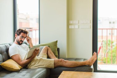 Genç adam evde kitap okuyor.