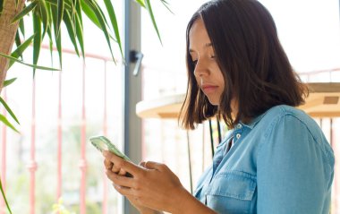 Genç ve güzel bir kadın telefonunu evde kullanıyor.