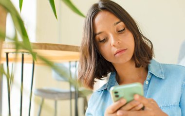 Genç ve güzel bir kadın telefonunu evde kullanıyor.