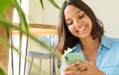 Genç ve güzel bir kadın telefonunu evde kullanıyor.