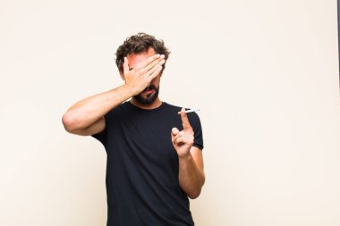 Genç sakallı adam sigara içiyor.