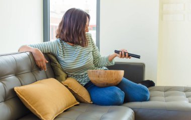 Genç ve güzel bir kadın evde televizyon izliyor.