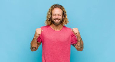 Sarışın adam son derece mutlu ve şaşırmış görünüyor, başarıyı kutluyor, bağırıyor ve zıplıyor.