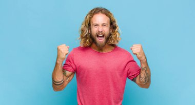 Sarışın adam sinirli bir ifadeyle ya da yumruklarıyla başarıyı kutlarken agresif bir şekilde bağırıyor.