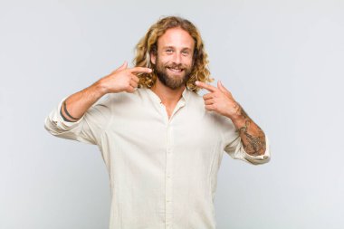 Sarışın adam kendinden emin bir şekilde gülümseyerek kendi geniş gülüşünü, pozitif, rahat, tatmin olmuş tavrını gösteriyor.