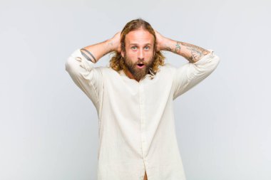 Sarışın adam heyecanlı ve şaşırmış görünüyor, ağzı açık, elleri başının üstünde, şanslı bir kazanan gibi hissediyor.