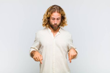 Sarışın ve ağzı açık bir adam iki eliyle aşağıya bakıyor. Şok olmuş, şaşırmış ve şaşırmış görünüyor.