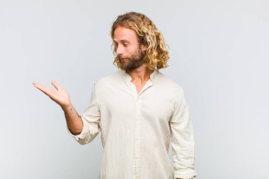 Sarışın bir adam kendini mutlu hisseder ve gelişigüzel gülümser. Elinde tuttuğu bir nesneye ya da konsepte bakar.