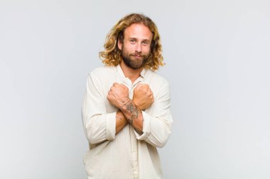 Sarışın adam sevinçle gülümsüyor ve kutluyor, yumruklarını sıkmış ve kollarını kavuşturmuş, mutlu ve pozitif hissediyor.