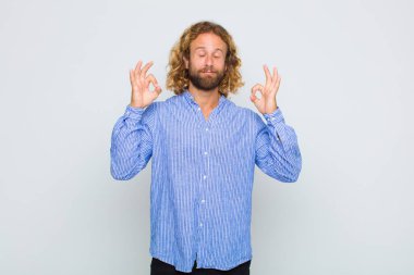 Sarışın adam konsantre olmuş ve meditasyon yapıyor. Tatmin olmuş ve rahatlamış hissediyor. Düşünüyor ya da bir seçim yapıyor.