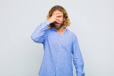 Sarışın adam şok olmuş, korkmuş ya da korkmuş görünüyordu. Yüzü elle kaplıydı ve parmaklarının arasından bakıyordu.