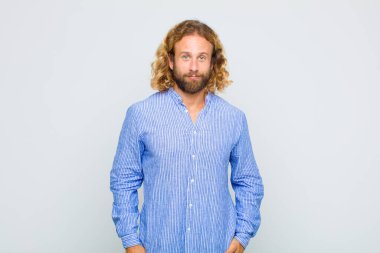 Sarışın adam pozitif ve kendinden emin gülümsüyor. Tatmin olmuş, arkadaş canlısı ve mutlu görünüyor.