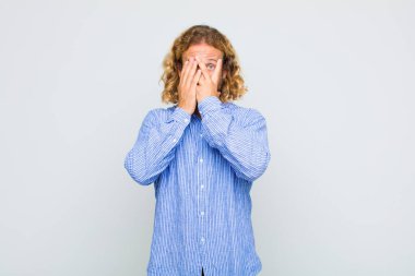 Sarışın adam korkmuş ya da utanmış hissediyor. Gözleri yarı kapalı ya da elleri açık bir şekilde dikizliyor.