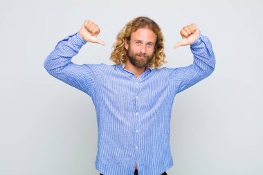 Sarışın adam gururlu, kibirli ve kendinden emin, tatmin olmuş ve başarılı görünüyor, kendini işaret ediyor.