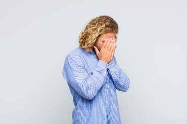 Sarışın bir adam, üzgün, hayal kırıklığına uğramış bakışlarıyla gözlerini kapatıyor, ağlıyor, yan gözle bakıyor.