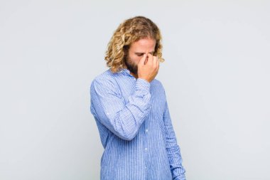 Sarışın bir adam stresli, mutsuz ve hayal kırıklığına uğramış, alnına dokunmuş ve şiddetli baş ağrısı çeken.