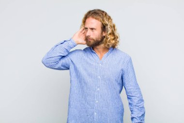 Sarışın adam ciddi ve meraklı görünüyor, dinliyor, gizli bir konuşma veya dedikodu duymaya çalışıyor, kulak misafiri oluyor.