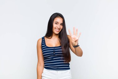 Genç bir kadın gülümsüyor ve arkadaş canlısı görünüyor, 4 ya da 4 numarayı gösteriyor, eli önde, geriye doğru sayıyor.