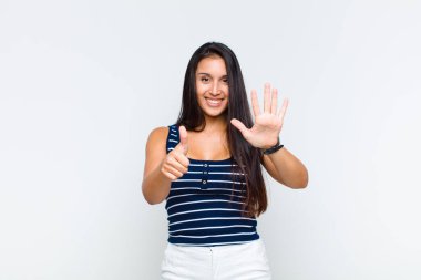 Genç bir kadın gülümsüyor ve arkadaş canlısı görünüyor, altı ya da altıncı numarayı gösteriyor, eli önde, geriye doğru sayıyor.