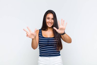 Genç bayan gülümsüyor ve arkadaş canlısı görünüyor, 8 ya da 8 numarayı gösteriyor, elleri önde, geri sayıyor.