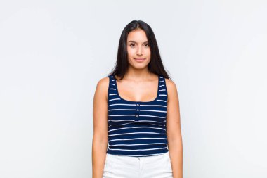 Genç bayan pozitif ve kendinden emin bir şekilde gülümsüyor, tatmin olmuş, arkadaş canlısı ve mutlu görünüyor.