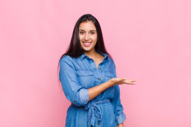 Neşeli bir şekilde gülümseyen genç bir kadın, mutlu hissediyor ve fotokopi alanında avucunun içinde bir konsept gösteriyor.