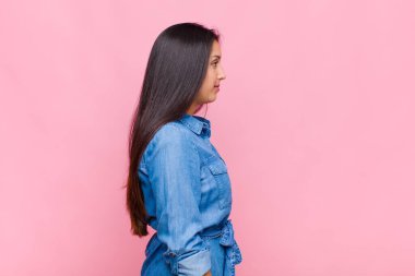 Profil görünümlü genç kadın ilerideki boşluğu kopyalamaya çalışıyor, düşünüyor, hayal ediyor ya da hayal kuruyor.