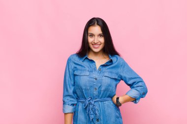 Genç bayan pozitif ve kendinden emin bir şekilde gülümsüyor, tatmin olmuş, arkadaş canlısı ve mutlu görünüyor.