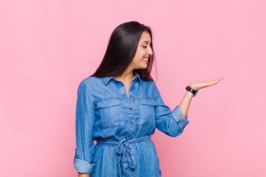 Genç bir kadın kendini mutlu hissediyor ve gelişigüzel gülümsüyor. Elinde tuttuğu bir nesneye ya da konsepte bakıyor.