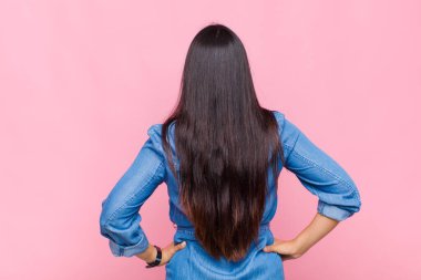 Genç bir kadın kafası karışık ya da dolgun ya da şüphe ve soru dolu, merak ediyor, elleri kalçasında, dikiz aynasından