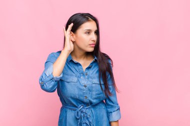 Genç bir kadın ciddi ve meraklı görünüyor, dinliyor, gizli bir konuşma veya dedikodu duymaya çalışıyor, kulak misafiri oluyor.