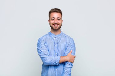 Genç adam utangaç ve neşeli bir şekilde gülüyor, arkadaş canlısı ve olumlu ama güvensiz bir tavırla.