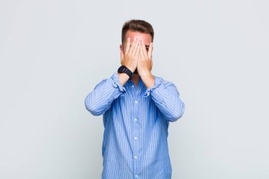 Genç adam elleriyle yüzünü kapatıyor, parmaklarının arasından şaşkın bir ifadeyle yan tarafa bakıyor.