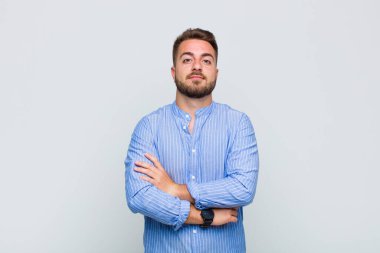 Genç adam omuz silkiyor, kafası karışık ve kararsız, kolları bağlı ve şaşkın bir şekilde şüpheli bakıyor.