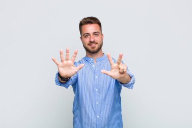 Genç adam gülümsüyor ve arkadaş canlısı görünüyor, 8 ya da 8 numarayı gösteriyor, elleri önde, geriye doğru sayıyor.