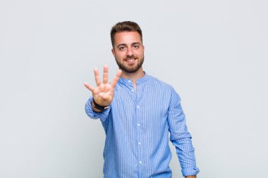 Genç adam gülümsüyor ve arkadaş canlısı görünüyor, dört ya da dört numarayı gösteriyor, eli önde, geriye doğru sayıyor.